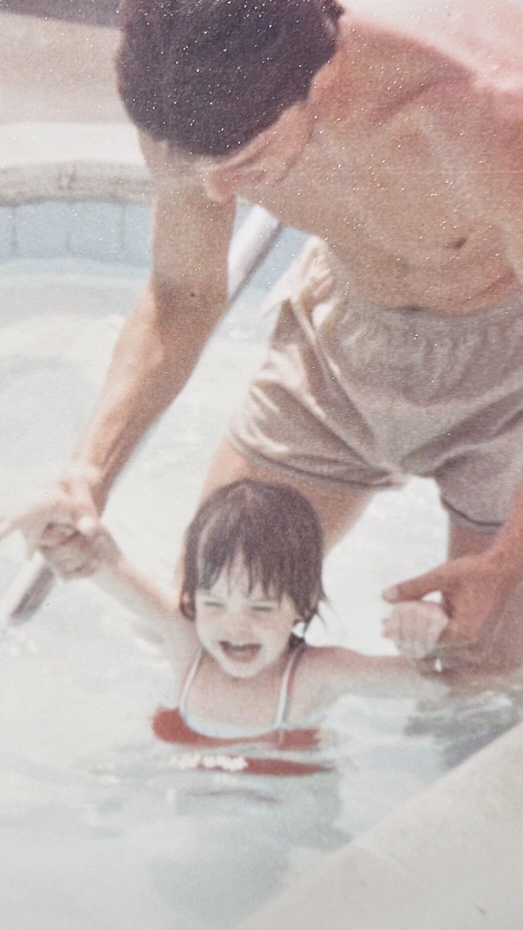 Shannon at age 2 with her dad, Brandt in the pool. He is clutching her arms and holding her above the water. | Mr.Countertops