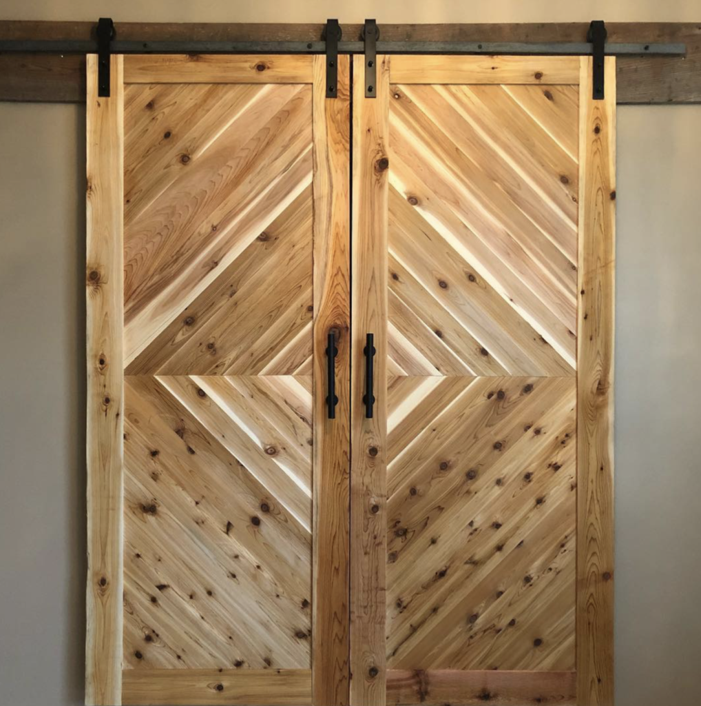 Handcrafted knotty wood barn door featuring a zig-zag herringbone pattern and rustic iron sliding hardware.